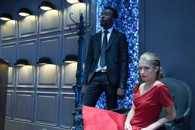 The director explaining a scene to the actors on set. They are standing in a meticulously designed set, complete with props and lighting equipment. The director is gesturing emphatically, conveying their vision for the scene.