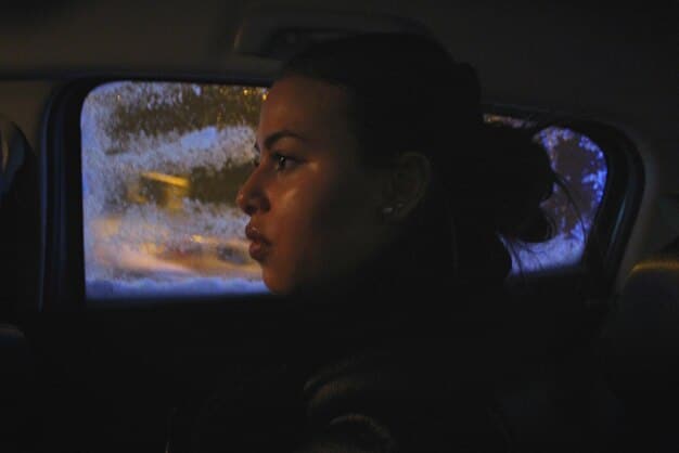 A close-up shot of a thoughtful woman's face, bathed in the soft glow of a screen, reflecting a complex emotion; she is immersed in a dramatic scene from a TV series.