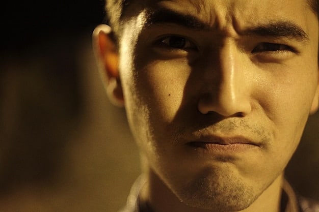 A close-up, low-light photograph of an actor's face, conveying deep emotion without revealing specific narrative context. The lighting creates strong contrasts, emphasizing the character's internal struggle or contemplation.