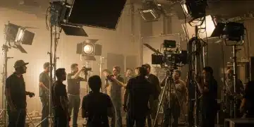 Film crew members from the grip and electric department meticulously setting up complex lighting equipment on a movie set.